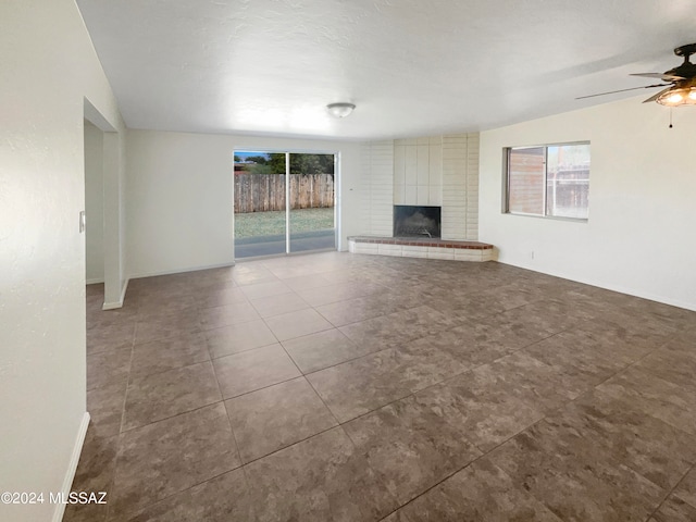 unfurnished living room featuring ceiling fan, lofted ceiling, a wealth of natural light, and a brick fireplace