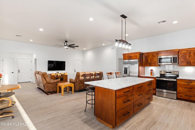 kitchen featuring stainless steel appliances, a breakfast bar area, hanging light fixtures, light hardwood / wood-style flooring, and a center island