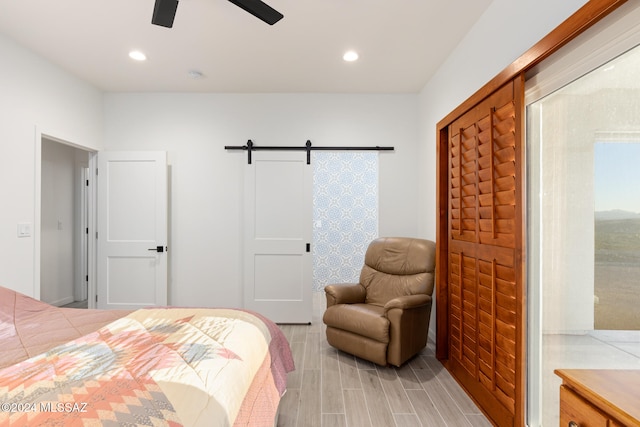 bedroom with light wood-type flooring, a barn door, and ceiling fan