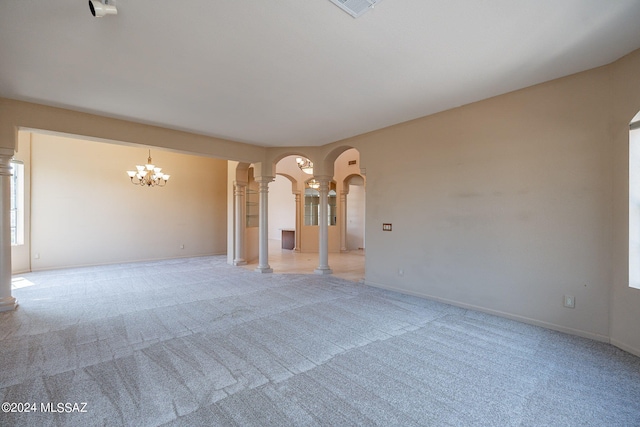 unfurnished living room featuring light carpet, a chandelier, and decorative columns