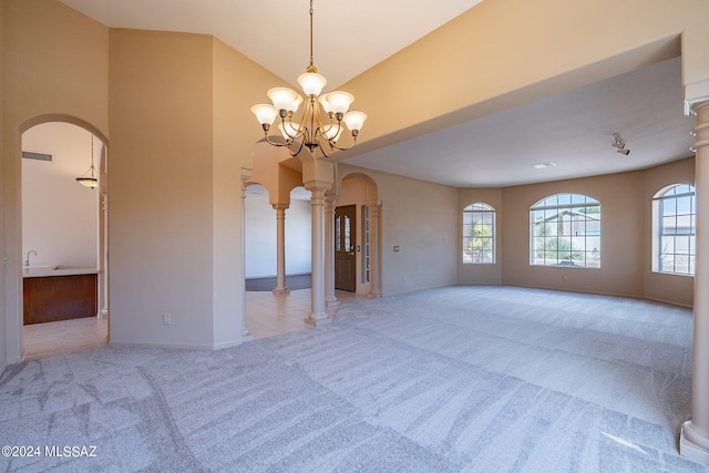 carpeted empty room with a notable chandelier and decorative columns