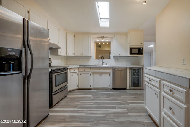 kitchen featuring white cabinets, sink, wine cooler, a skylight, and stainless steel appliances