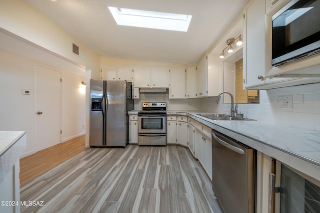 kitchen featuring lofted ceiling with skylight, white cabinets, sink, light hardwood / wood-style flooring, and stainless steel appliances