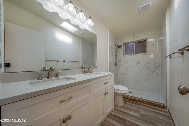 bathroom featuring a skylight, vanity, tiled shower, hardwood / wood-style flooring, and toilet