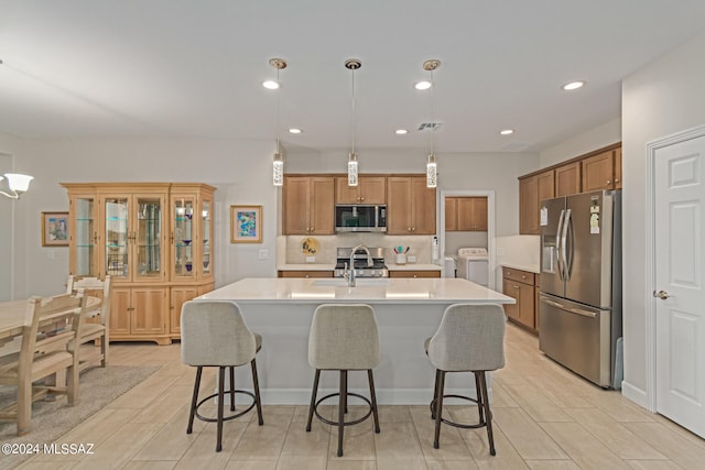 kitchen featuring a center island with sink, stainless steel appliances, hanging light fixtures, and washing machine and dryer