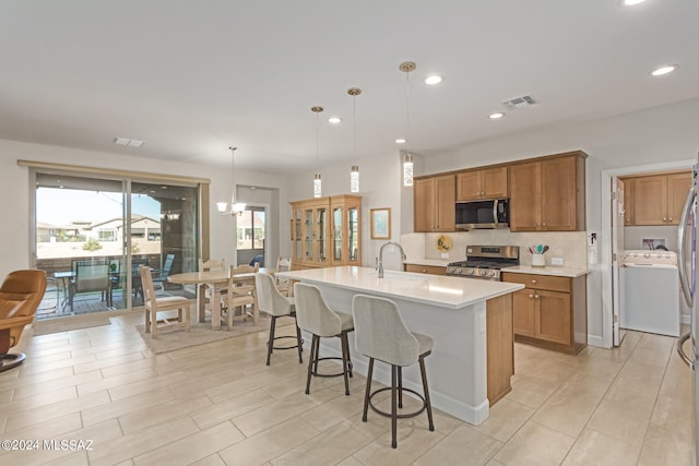 kitchen with a kitchen bar, hanging light fixtures, backsplash, a center island with sink, and appliances with stainless steel finishes