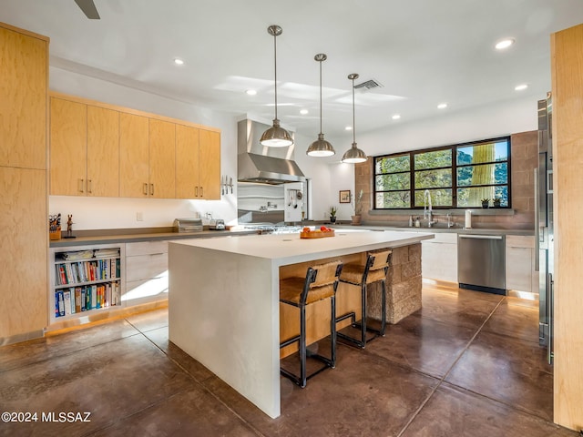 kitchen featuring wall chimney exhaust hood, stainless steel appliances, light brown cabinets, a center island, and hanging light fixtures