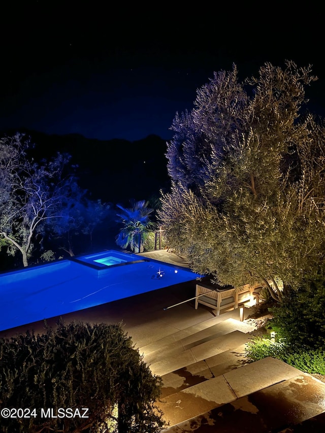 pool at night with an in-ground hot tub, a patio area, and an outdoor pool
