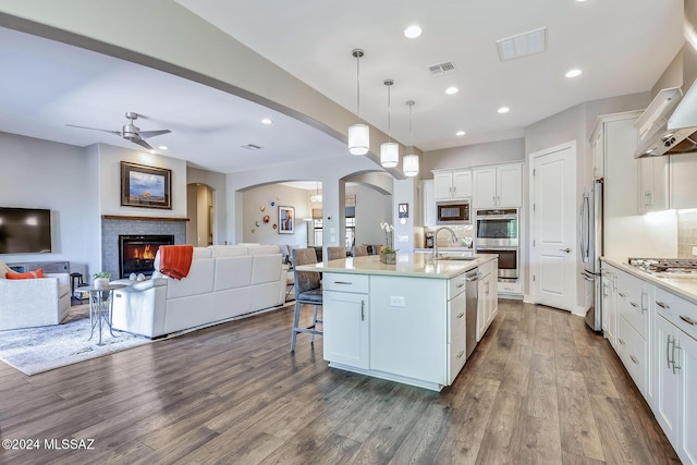 kitchen featuring decorative backsplash, appliances with stainless steel finishes, decorative light fixtures, a center island with sink, and white cabinets