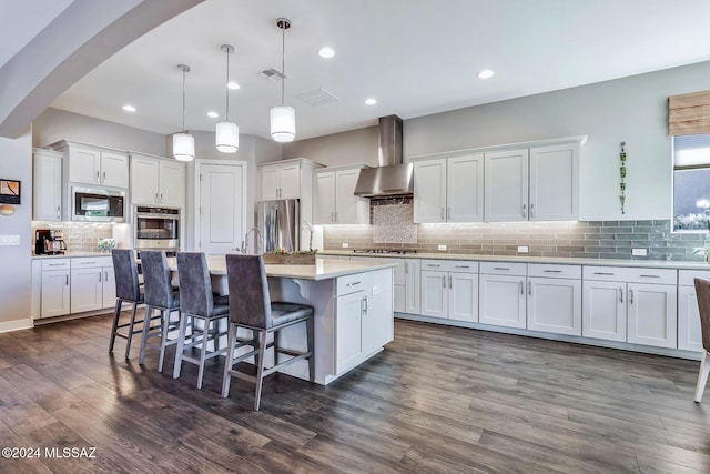 kitchen featuring white cabinets, wall chimney exhaust hood, pendant lighting, and appliances with stainless steel finishes