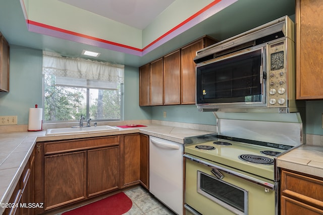 kitchen featuring light tile patterned floors, white dishwasher, electric stove, tile counters, and sink