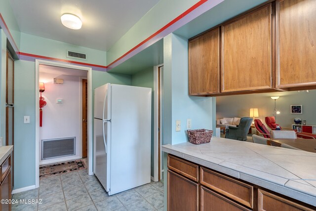 kitchen featuring white fridge, tile counters, and light tile patterned floors