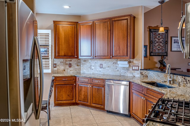 kitchen with light stone counters, stainless steel appliances, sink, hanging light fixtures, and light tile patterned flooring