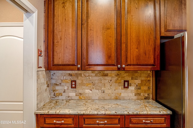 kitchen featuring backsplash, stainless steel refrigerator, and light stone counters