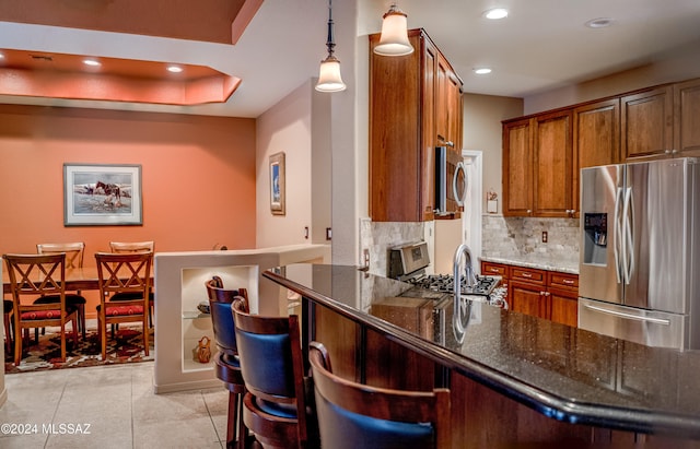 kitchen featuring pendant lighting, dark stone countertops, appliances with stainless steel finishes, tasteful backsplash, and kitchen peninsula