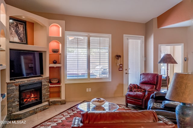 tiled living room featuring built in shelves and a stone fireplace