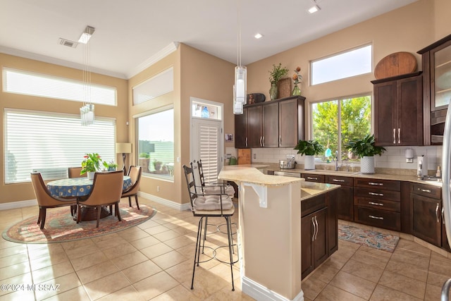 kitchen featuring visible vents, decorative backsplash, a kitchen breakfast bar, and dark brown cabinetry