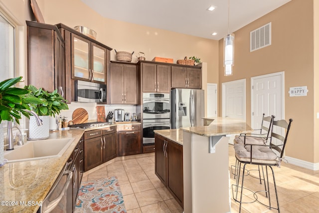 kitchen featuring dark brown cabinets, sink, light stone counters, hanging light fixtures, and appliances with stainless steel finishes