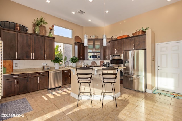 kitchen featuring a kitchen breakfast bar, dark brown cabinetry, stainless steel appliances, decorative backsplash, and light tile patterned flooring
