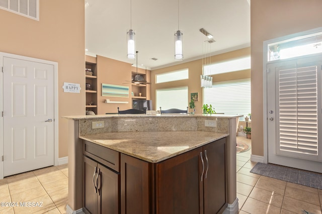 kitchen with dark brown cabinetry, pendant lighting, light stone countertops, and light tile patterned floors