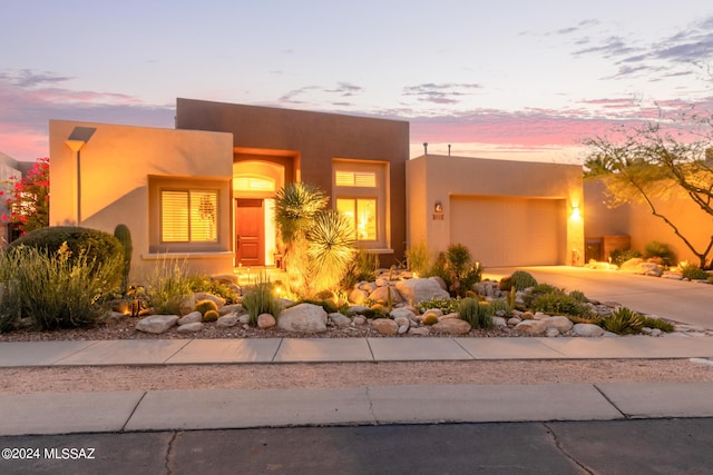 pueblo-style house with an attached garage, concrete driveway, and stucco siding