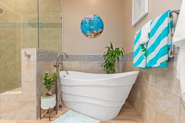 bathroom featuring wainscoting, tile walls, a tile shower, and a soaking tub