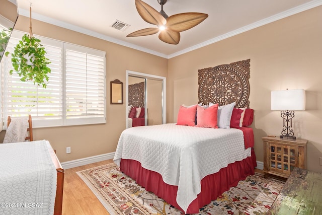 bedroom with visible vents, baseboards, a closet, ornamental molding, and wood finished floors