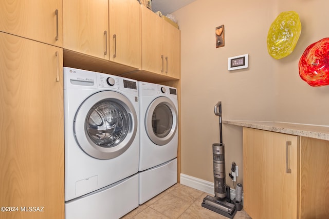 clothes washing area with light tile patterned flooring, washer and clothes dryer, and cabinets