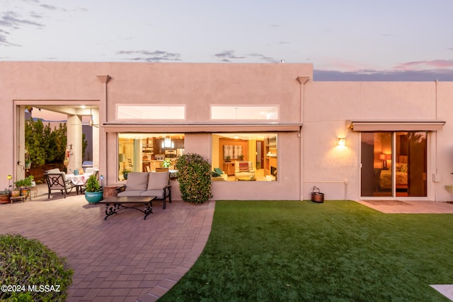 back house at dusk featuring a yard and a patio area