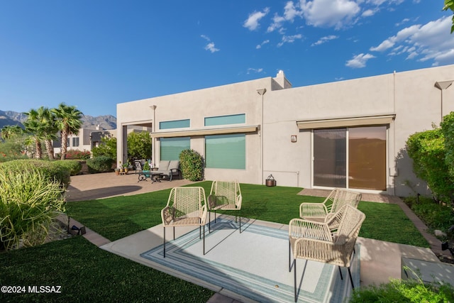 rear view of house with a patio, stucco siding, a mountain view, and a yard