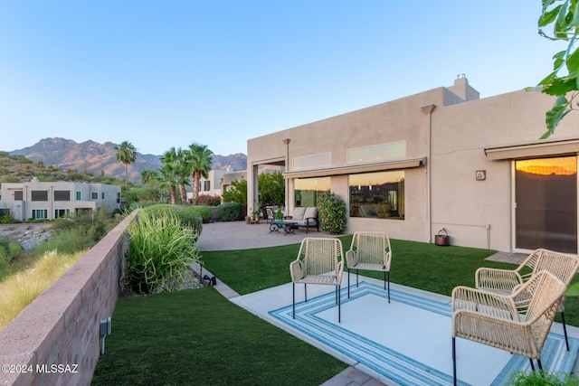 back of house with a yard, a mountain view, a patio, and stucco siding