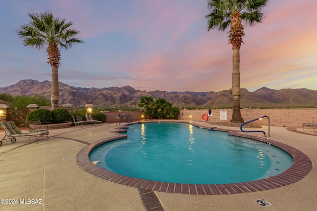 pool at dusk featuring a patio, a mountain view, and a fenced in pool