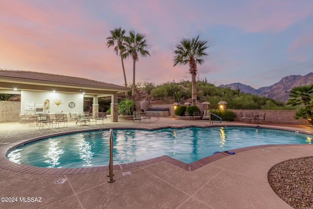pool at dusk featuring a patio, a community pool, a mountain view, and fence
