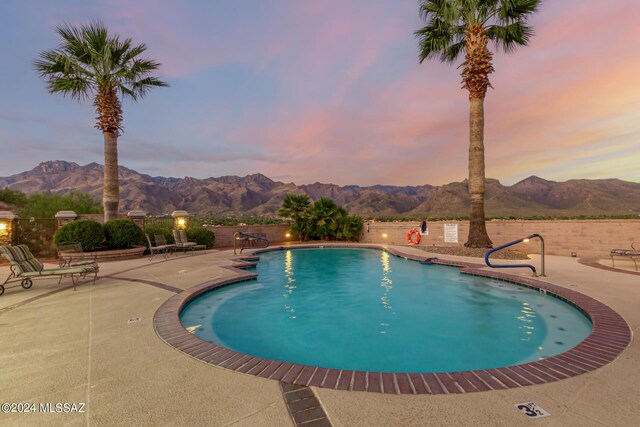 pool at dusk featuring a patio, a mountain view, and a fenced in pool