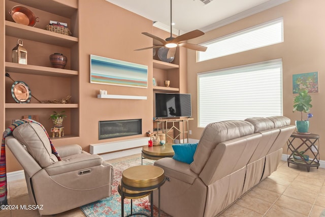 tiled living room featuring crown molding, ceiling fan, a glass covered fireplace, baseboards, and built in shelves