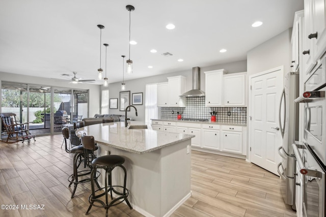 kitchen featuring light hardwood / wood-style floors, wall chimney exhaust hood, an island with sink, and white cabinets