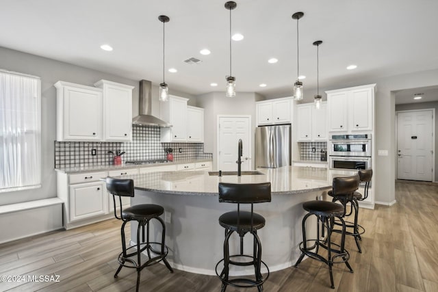 kitchen featuring wall chimney range hood, appliances with stainless steel finishes, a spacious island, white cabinetry, and sink