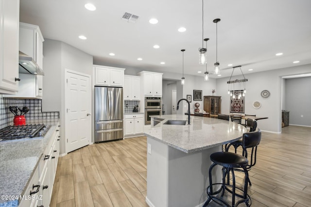 kitchen featuring wall chimney range hood, a spacious island, light wood-type flooring, sink, and stainless steel appliances