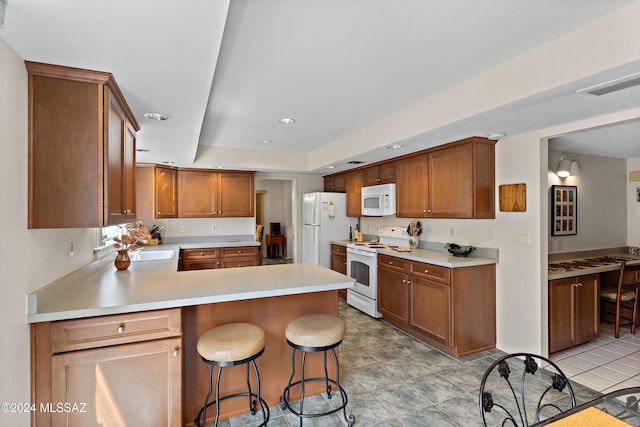 kitchen featuring kitchen peninsula, white appliances, sink, a breakfast bar area, and light tile patterned flooring