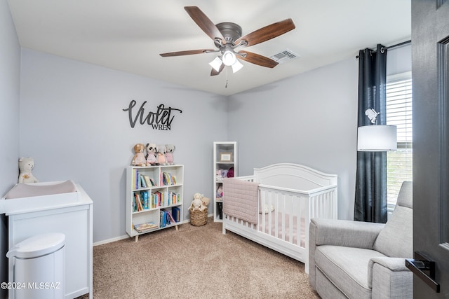 carpeted bedroom featuring a nursery area and ceiling fan