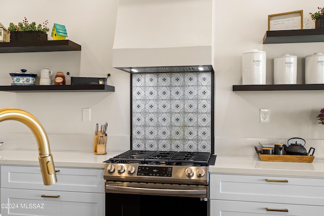 kitchen featuring decorative backsplash, white cabinetry, stainless steel range with gas stovetop, and light stone counters