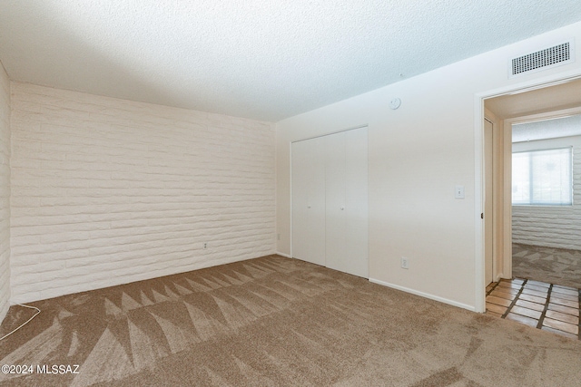 unfurnished bedroom featuring carpet, a closet, brick wall, and a textured ceiling