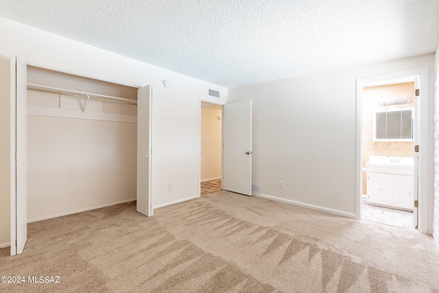 unfurnished bedroom featuring a textured ceiling, carpet flooring, ensuite bathroom, and a closet