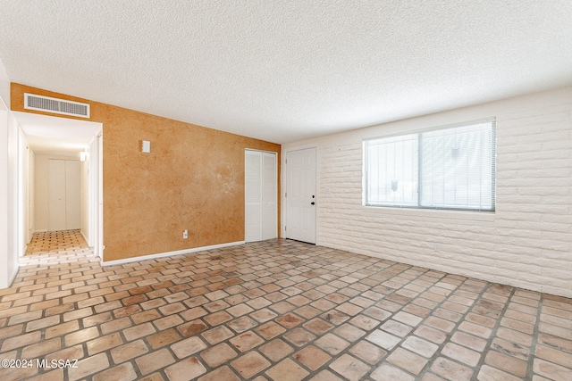 empty room featuring a textured ceiling and brick wall