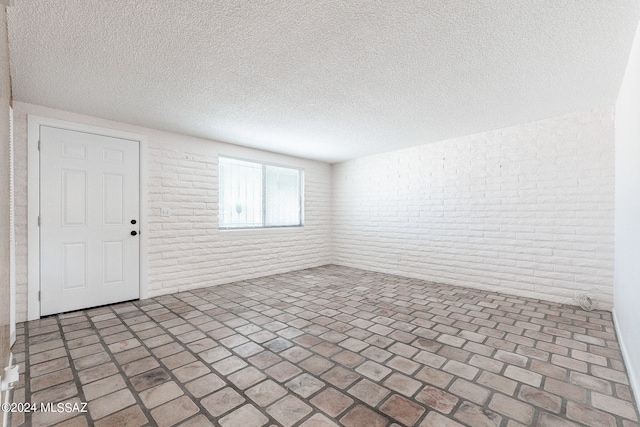 unfurnished room featuring a textured ceiling and brick wall