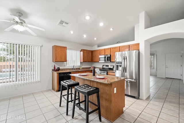 kitchen with a kitchen island, light stone countertops, ceiling fan, a breakfast bar, and appliances with stainless steel finishes