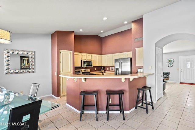 kitchen with a kitchen bar, appliances with stainless steel finishes, light tile patterned floors, high vaulted ceiling, and kitchen peninsula