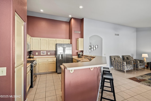 kitchen with light tile patterned floors, appliances with stainless steel finishes, kitchen peninsula, and a breakfast bar area