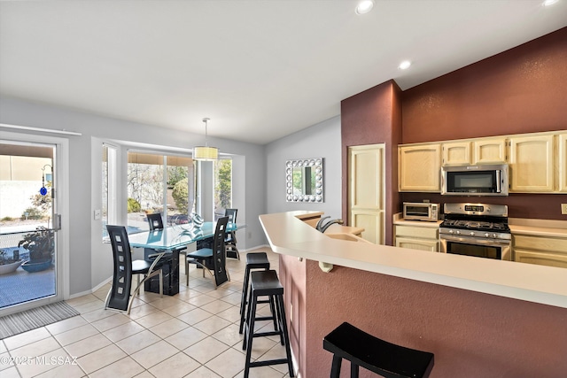 kitchen with vaulted ceiling, appliances with stainless steel finishes, decorative light fixtures, light tile patterned floors, and a kitchen bar