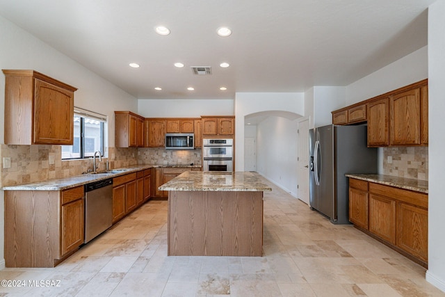 kitchen with arched walkways, a sink, light stone counters, a kitchen island, and appliances with stainless steel finishes